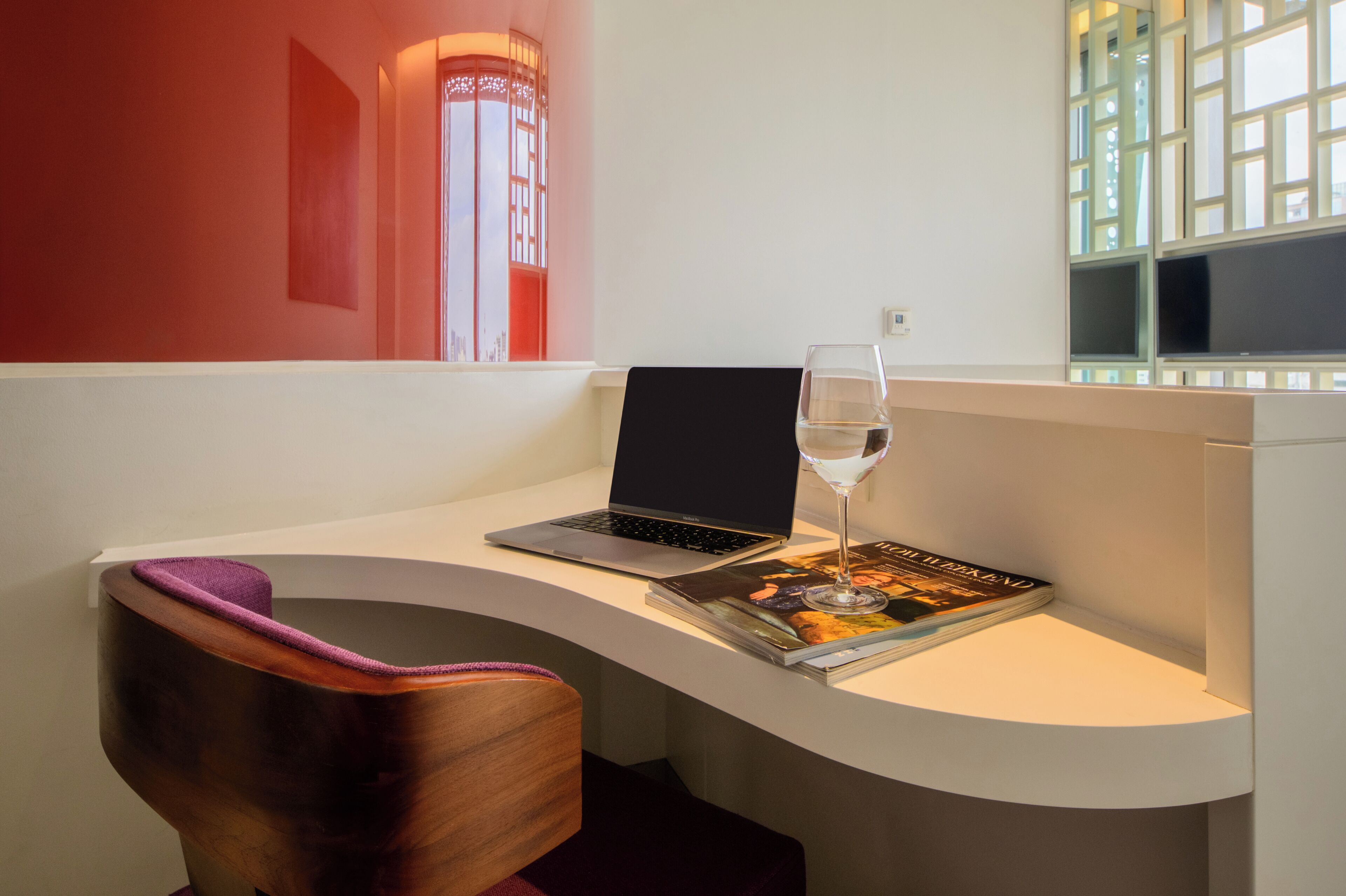 A modern room with a curved white desk, a laptop, a glass of water, and a magazine.