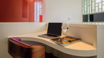A modern room with a curved white desk, a laptop, a glass of water, and a magazine.