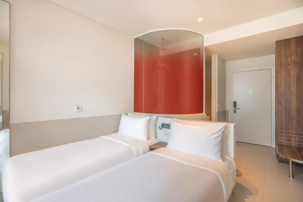 Een hotelkamer met twee bedden, een grote spiegel, een houten kledingkast en een deur naar een andere kamer.