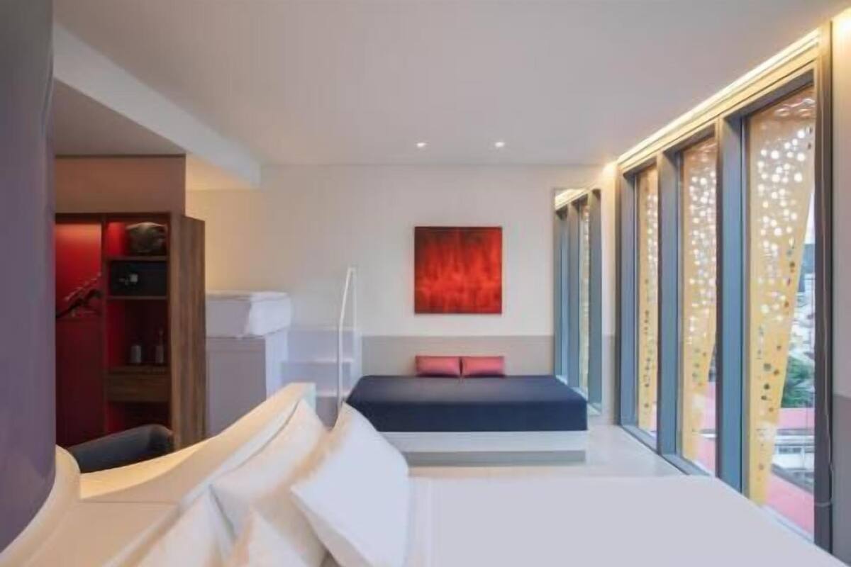 Een moderne slaapkamer met een bed, een rode accentmuur en een groot raam.