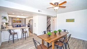 A modern kitchen with white cabinets, a wooden island, and a dining area with a wooden table and chairs. - LUXURY Living 5 (Yuma)