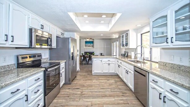 A modern kitchen with white cabinetry, granite countertops, stainless steel appliances, and a wooden floor. - LUXURY Living 5 (Yuma)