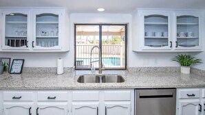 A kitchen with white cabinets, a granite countertop, a stainless steel sink, and a dishwasher. - LUXURY Living 5 (Yuma)