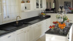 A modern kitchen with white cabinets, a black countertop, and a central island with fruit and glassware. - Sainte Maxime (Sainte-Maxime)
