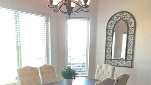 A dining room with a dark wooden table surrounded by four chairs, a chandelier, and a decorative mirror on the wall. - Luxury Living 6 (Yuma)