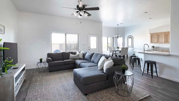 A spacious living room with a sectional sofa, a ceiling fan, and a kitchen area with bar stools. - Luxury Living 6 (Yuma)