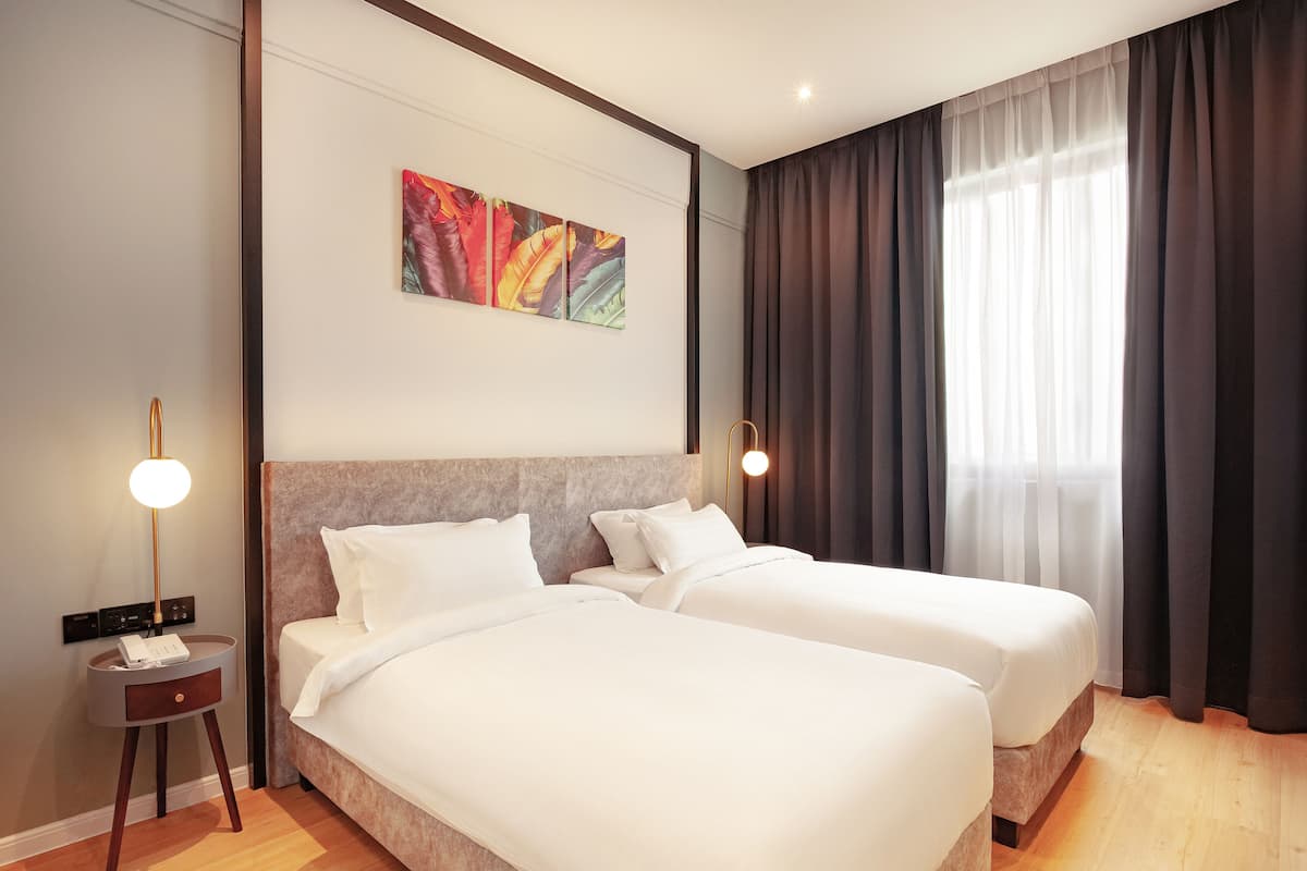 Hotelkamer met twee bedden, een modern hoofdeinde, een schilderij aan de muur en een groot raam met gordijnen.