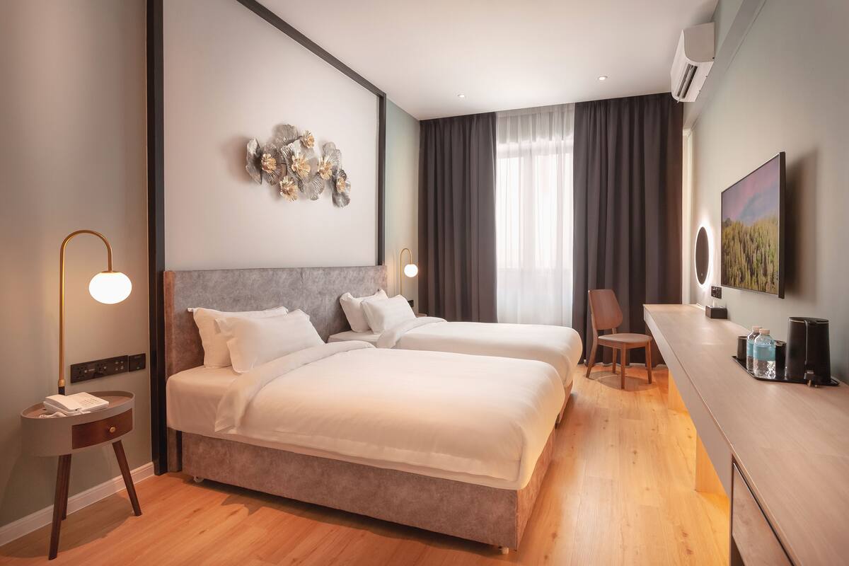 Een moderne hotelkamer met twee bedden, een bureau en een groot raam met gordijnen.