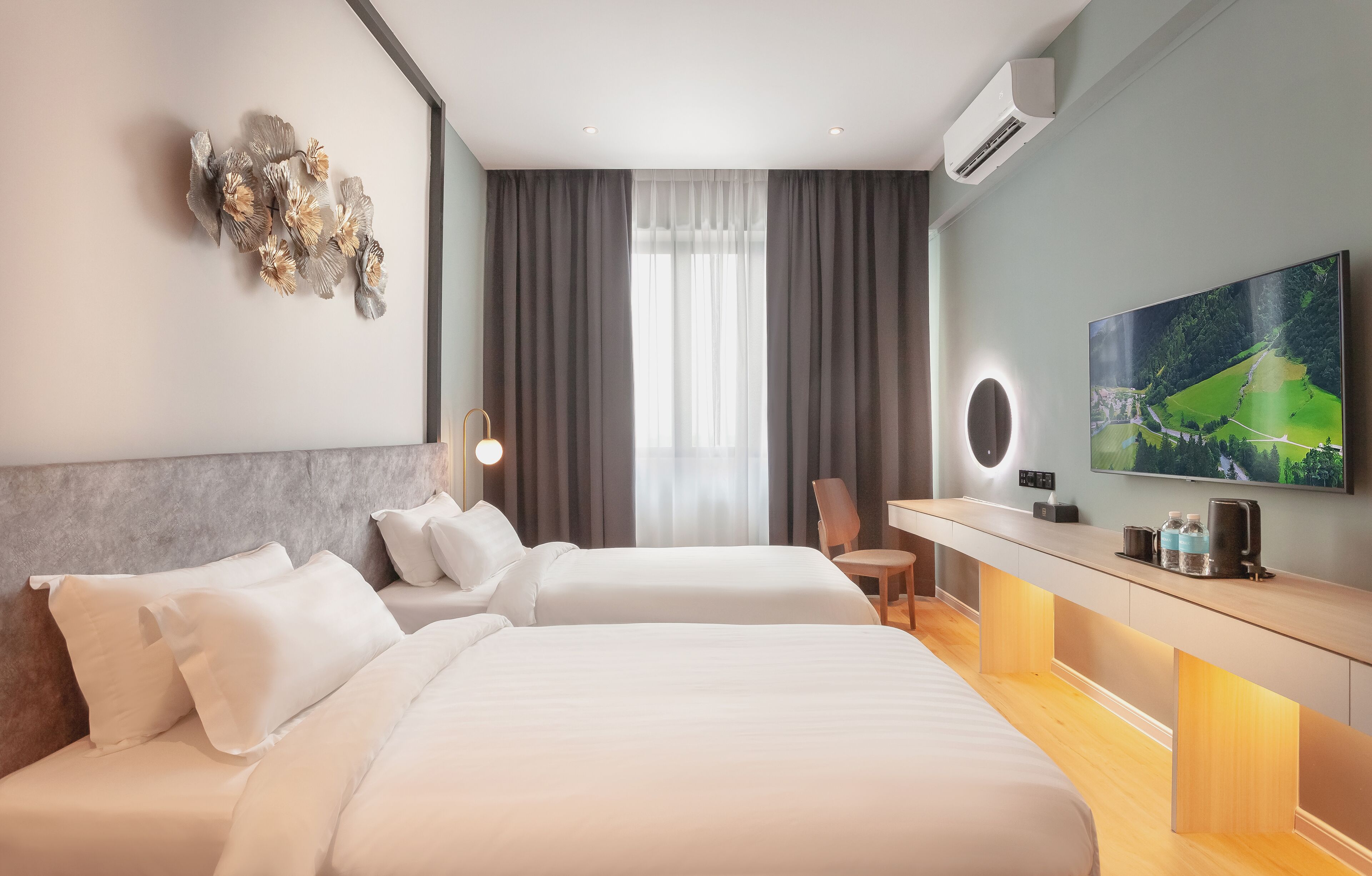 A modern hotel room with two beds, a desk, a chair, a large TV, and a decorative wall piece.
