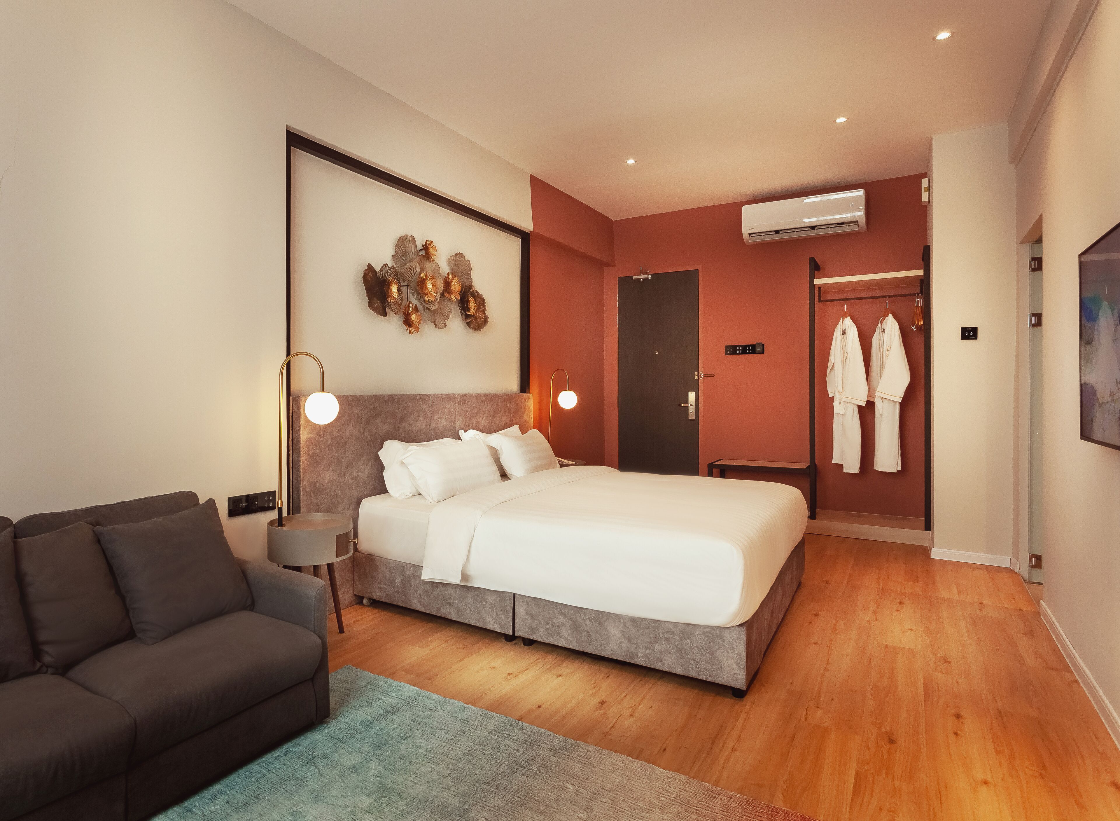 A modern hotel room with a large bed, a sofa, a desk, and an air conditioning unit.