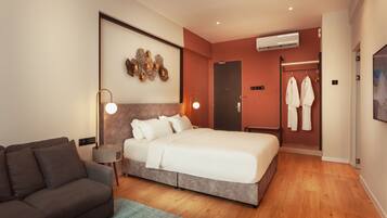 A modern hotel room with a large bed, a sofa, a desk, and an air conditioning unit.