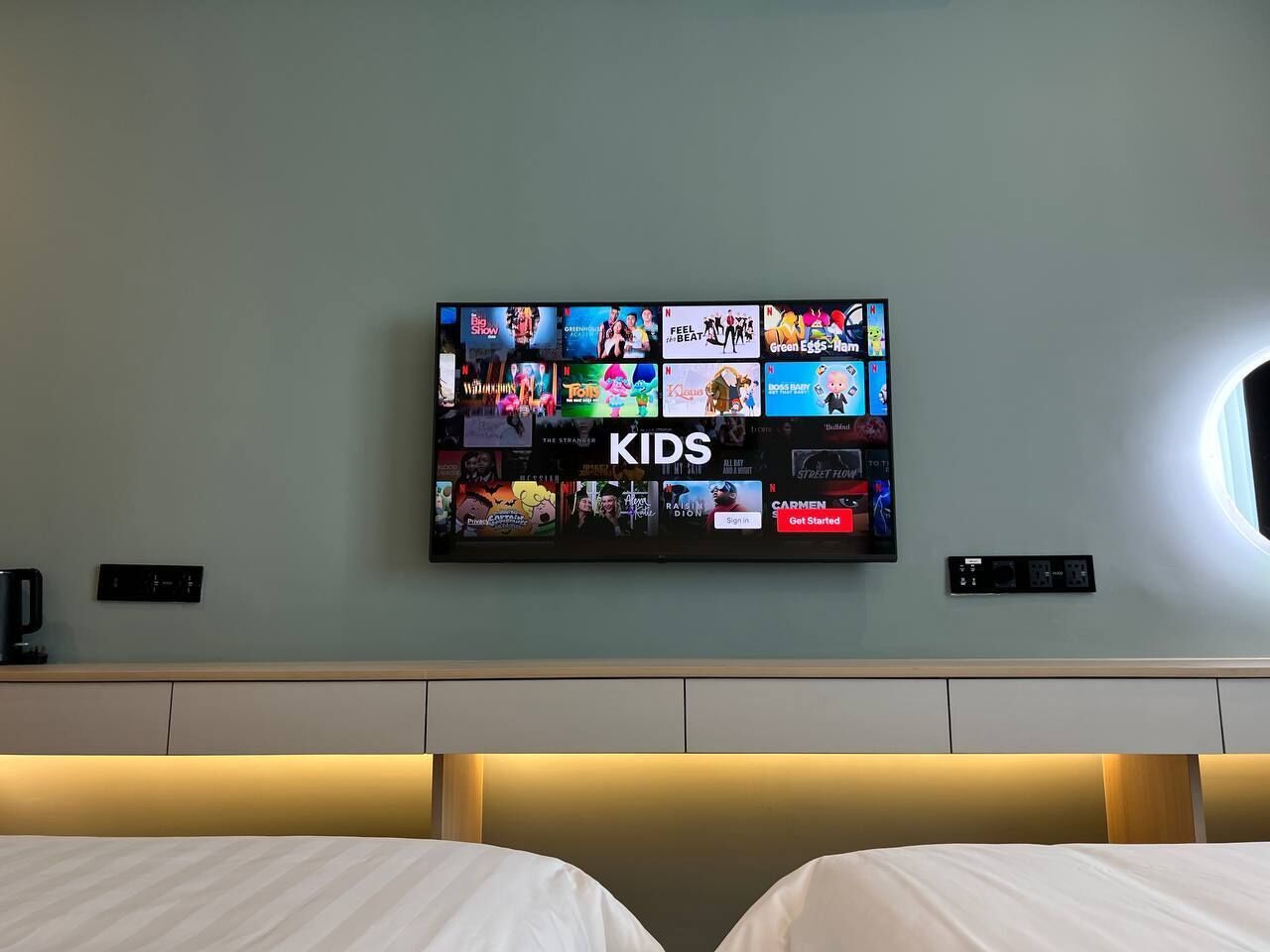 A hotel room with a TV displaying various children's shows and a bed with white linens.