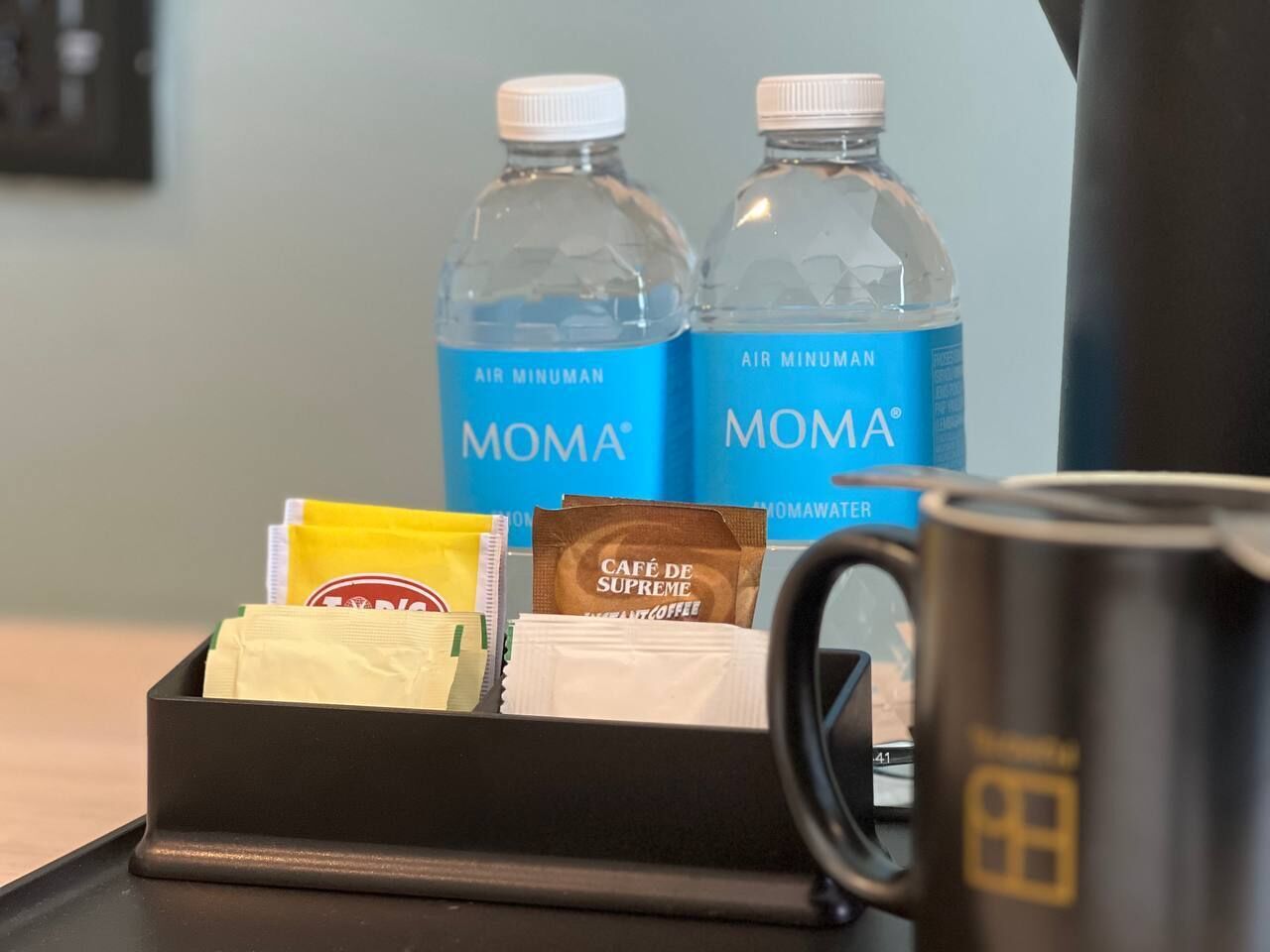 A coffee station with two MOMA water bottles, a coffee mug, and coffee packets.