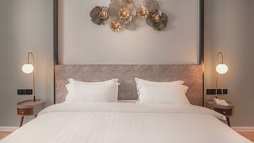 Una cama bien hecha con ropa de cama blanca, un cabecero moderno y un elemento decorativo en la pared sobre ella. Hay dos mesitas de noche con lámparas a cada lado de la cama.