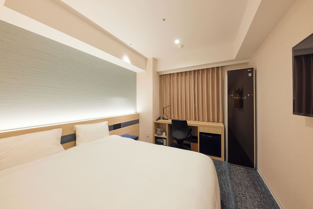 Une chambre d’hôtel avec un grand lit, un bureau avec une chaise, une armoire et une porte coulissante.