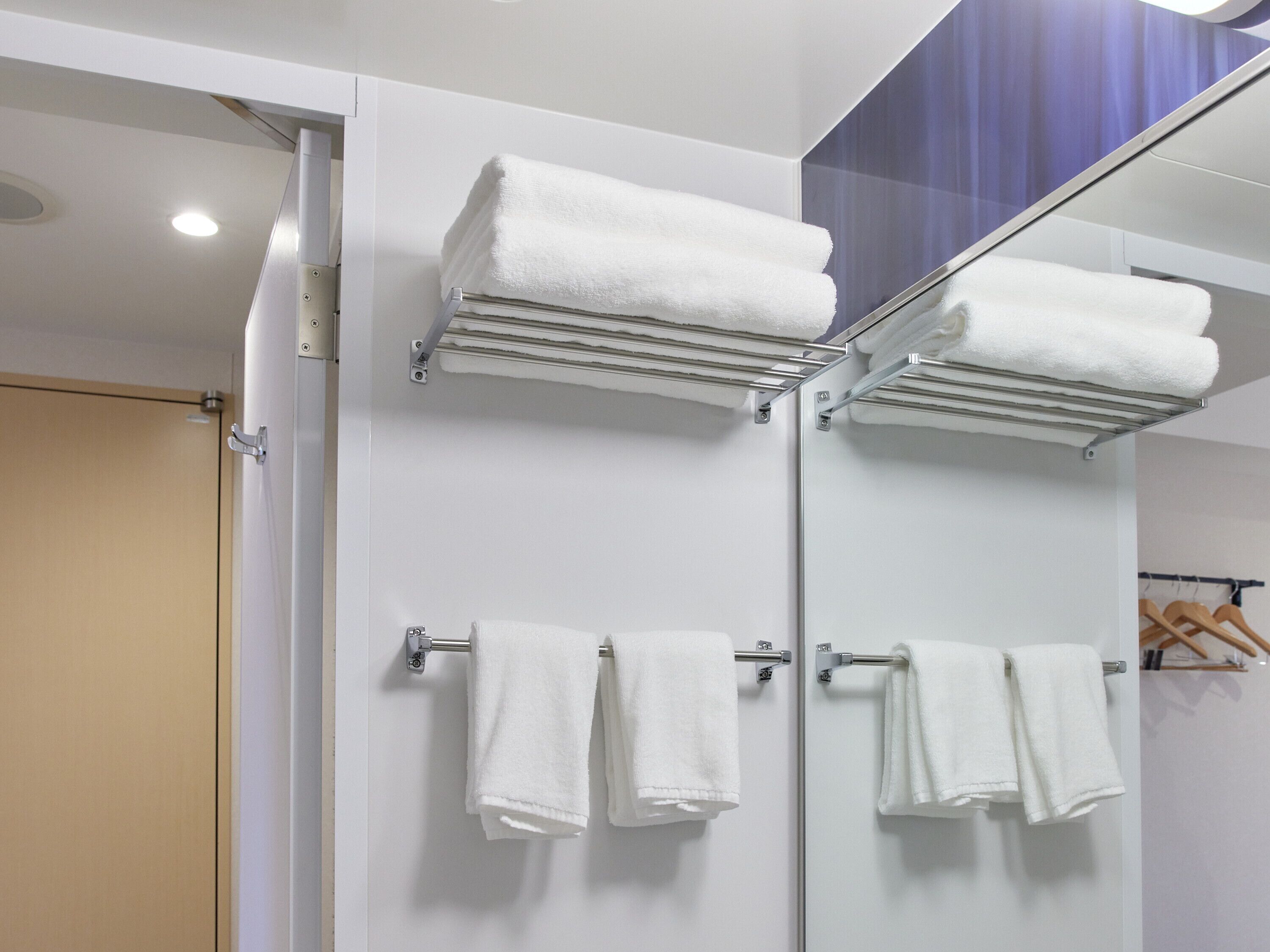 Un baño moderno con cabina de ducha de vidrio, toallas blancas en un perchero y una puerta de madera.