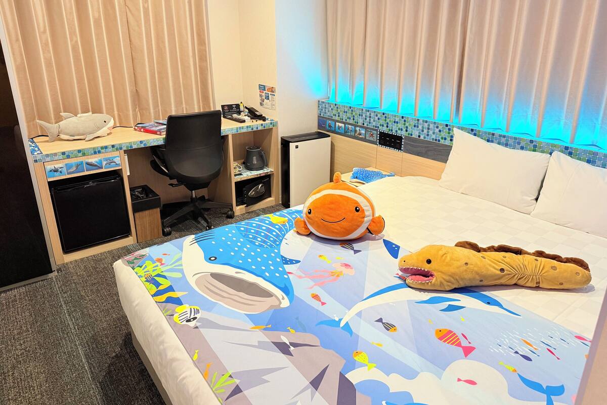 Une chambre d’hôtel équipée d’un lit, d’un bureau, d’une chaise, d’un petit réfrigérateur et d’une table de chevet.