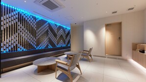 Een modern interieur met een zithoek, bestaande uit ronde tafels en houten stoelen, een decoratieve wand met blauwe verlichting en een houten deur op de achtergrond.