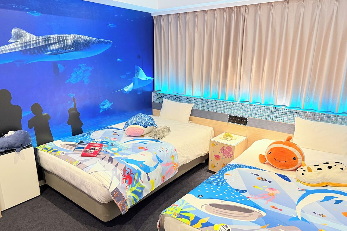 Une chambre d’hôtel avec deux lits, un grand mur décoré d’un aquarium et une vue sur l’océan.