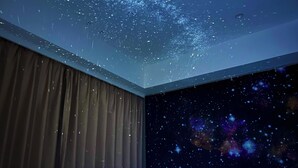 Een kamer met een sterrenhemelplafond en een muurschildering van een melkweg.