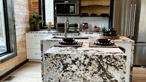 Una cocina moderna con paredes de madera, una isla de granito, electrodomésticos de acero inoxidable y salpicadero con mosaicos en espiga.