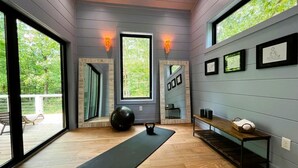 Um estúdio de yoga moderno com piso de madeira, janelas amplas e um banco de madeira com um cesto.