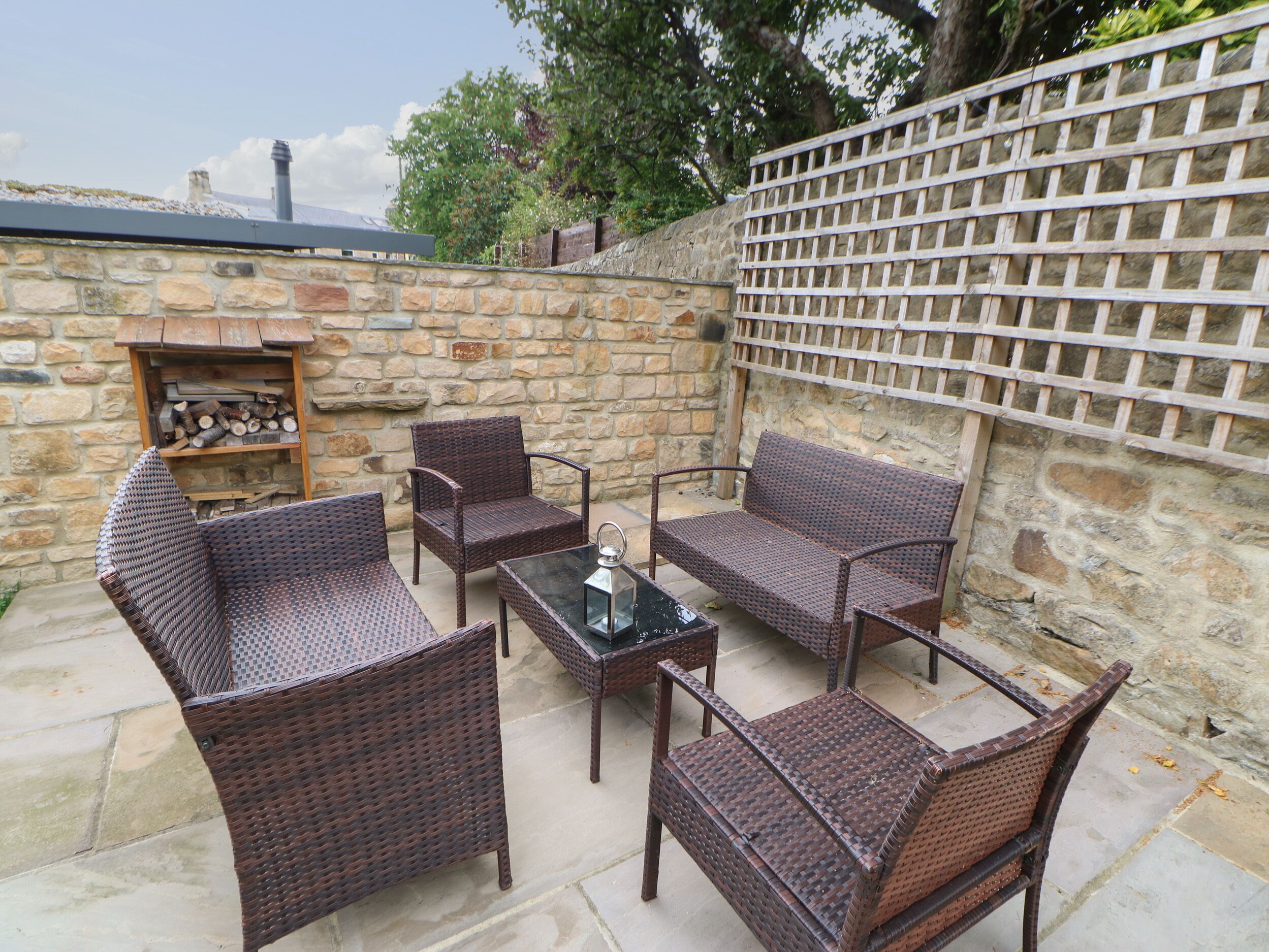 Een terras buiten met rieten meubilair, een glazen tafel en een stenen muur.
