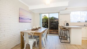 Une cuisine moderne dotée d’une grande fenêtre, un coin repas avec une table en bois et des chaises blanches, et un comptoir de cuisine avec des tabourets.