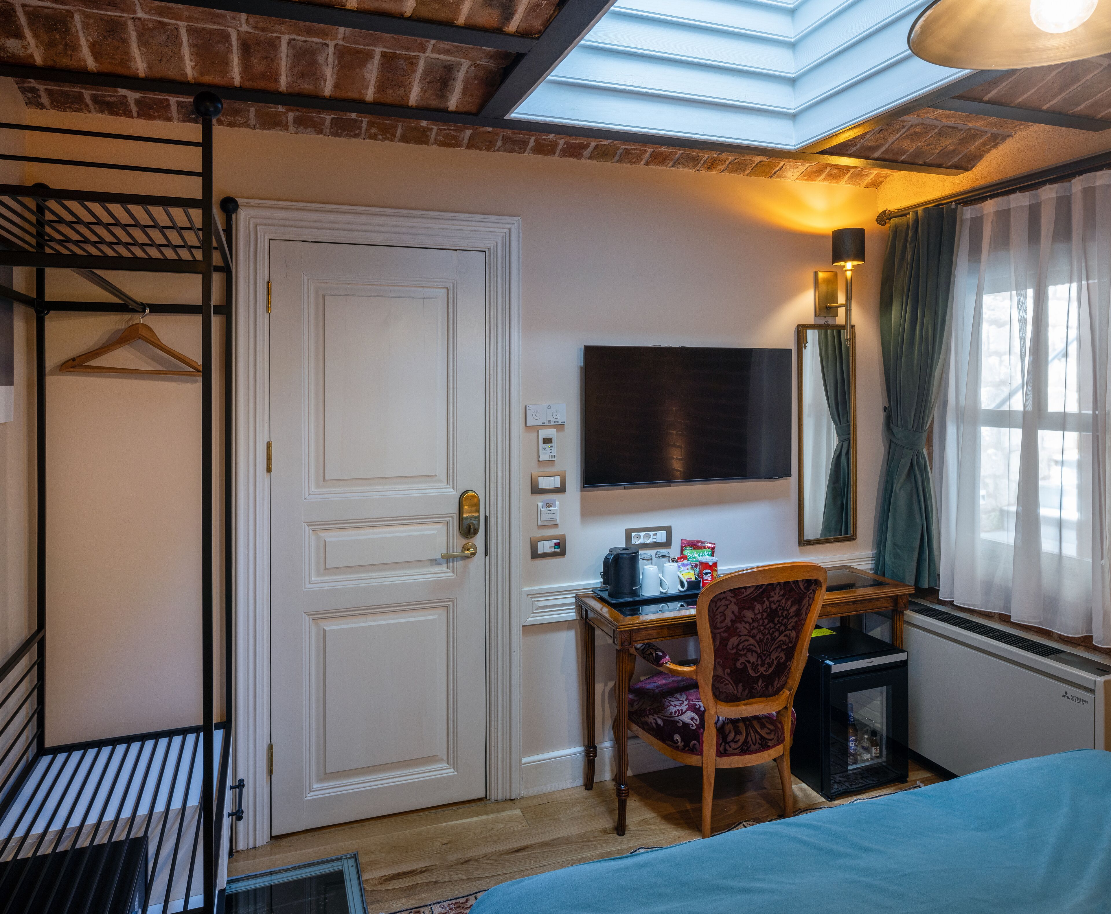 A hotel room with a bed, a desk with a chair, a TV, a heater, and a wardrobe.