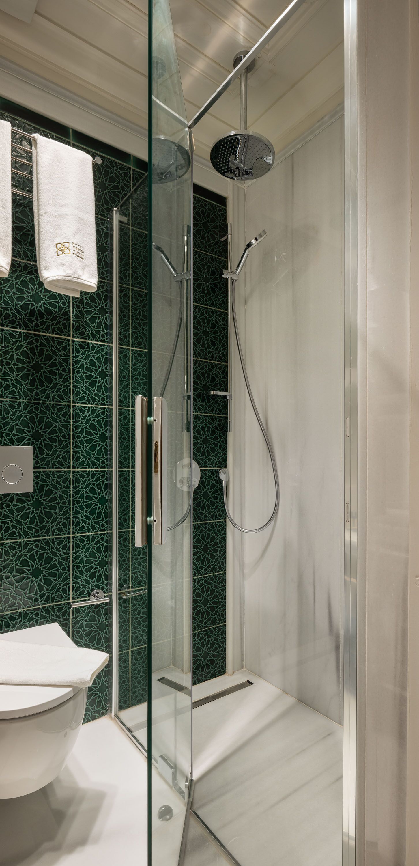 A modern bathroom with a glass-enclosed shower, a white sink, and green patterned tiles.