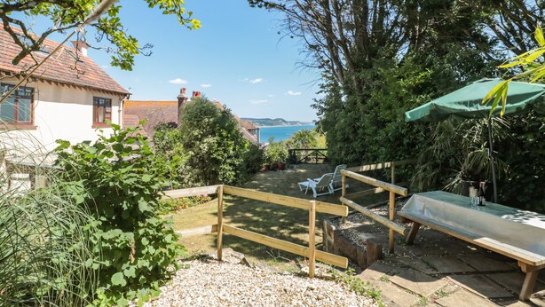 A garden with a wooden fence, a bench, and a table with a green umbrella. - Heselwood (Lyme Regis)