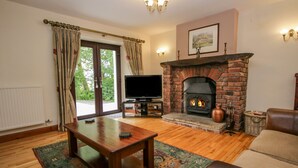 A living room with a fireplace, a television, and a leather sofa. - Ewedale Farm (Ulverston)