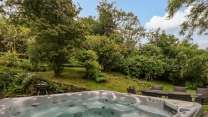 A hot tub surrounded by lush greenery and a stone wall. - Ewedale Farm (Ulverston)