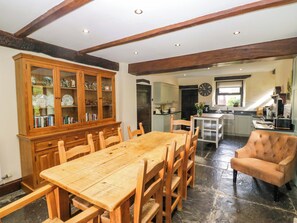 Un coin repas avec une table et des chaises en bois, un buffet avec des portes en verre, et une cuisine en arrière-plan.