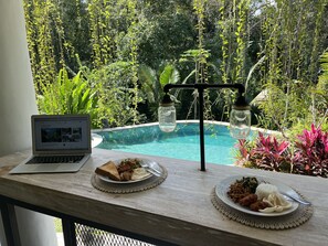 Un ordinateur portable est posé sur une table, offrant une vue sur une piscine et une végétation luxuriante.