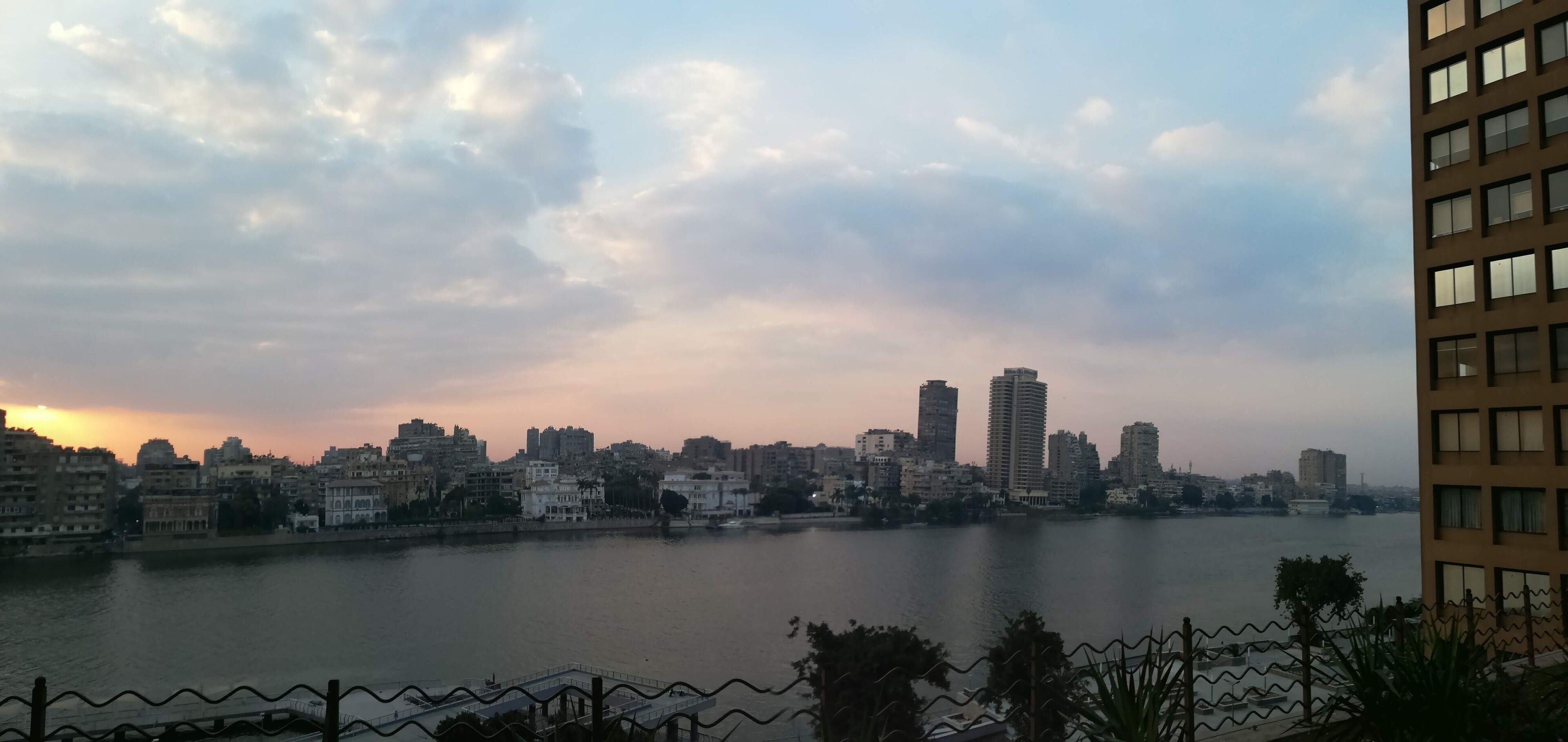 A city skyline with a river in the foreground, featuring a mix of modern and older buildings.