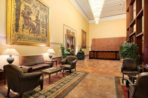 A lobby with a checkered sofa, armchairs, a coffee table, a reception desk, and a large wall painting.