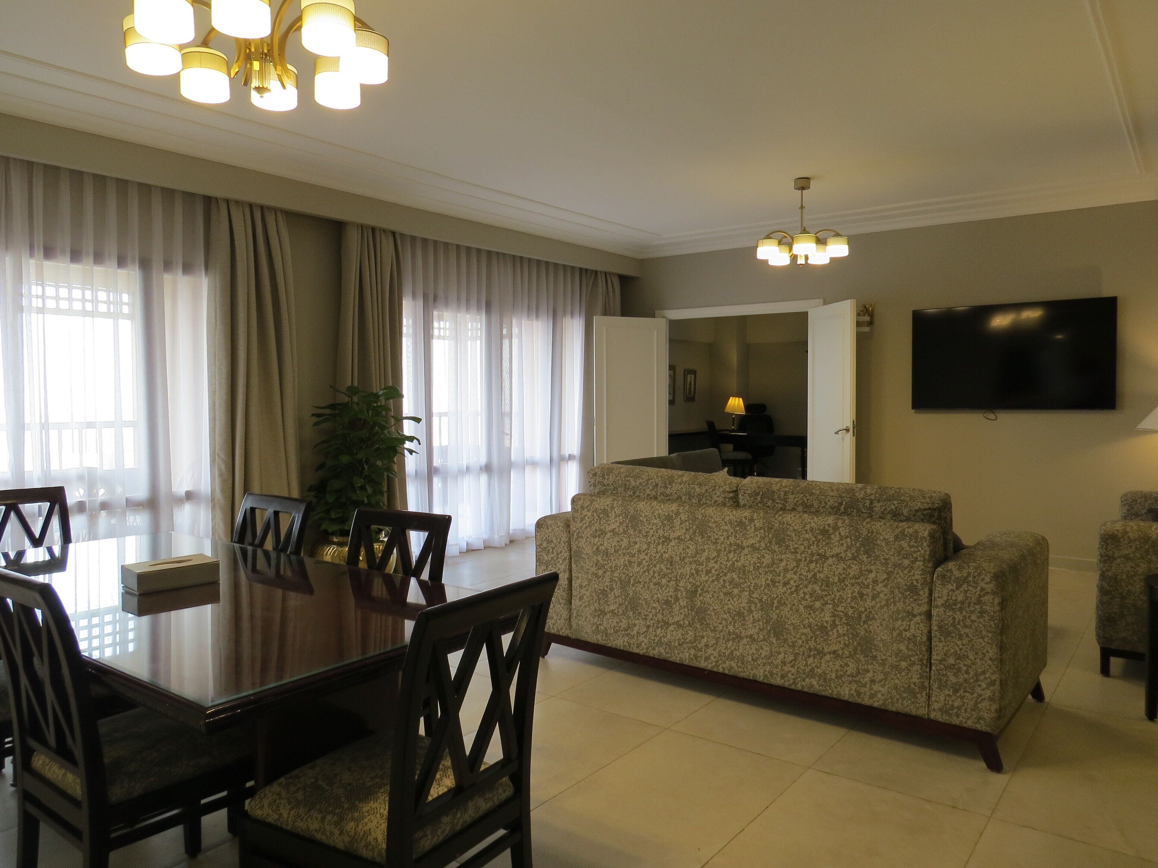 Una sala de estar con sofá, televisor, mesa de comedor, sillas y una araña.