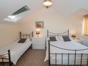 A bedroom with two beds, a small white dresser, a mirror, and a skylight. - The Coach House (Lyme Regis)