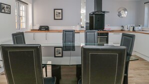 Une cuisine moderne dotée d’un îlot central, de meubles blancs et d’un coin repas avec une table et des chaises en verre.