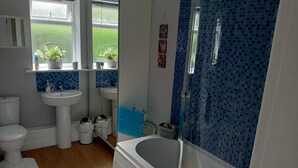 Kylpyhuoneessa on kylpyamme, kaksi pesuallasta, wc ja ikkuna, jossa on kasveja.