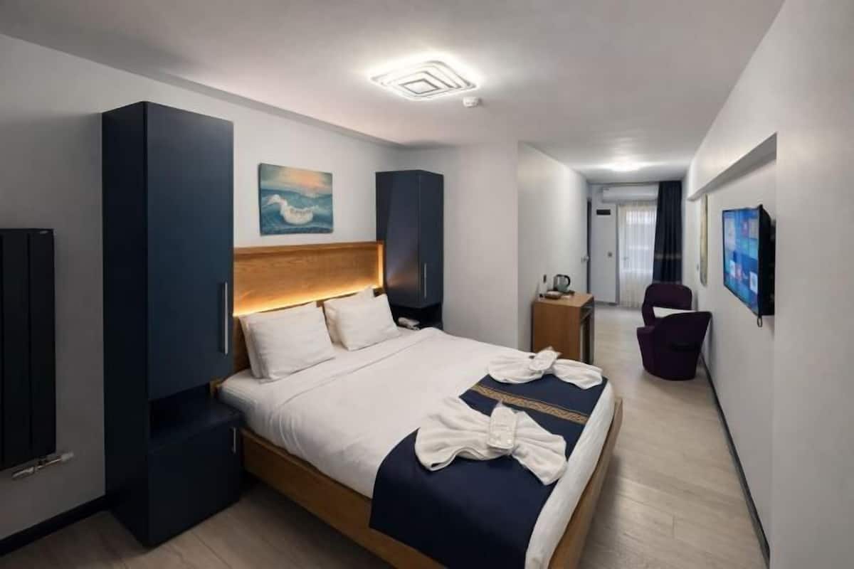 A modern hotel room with a large bed, a flat-screen TV, a desk, and a chair.