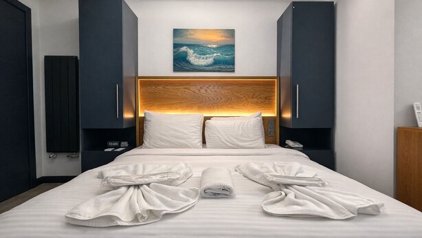 Habitación de hotel con una cama, un cuadro de una ola, cabecera de madera y un reloj.