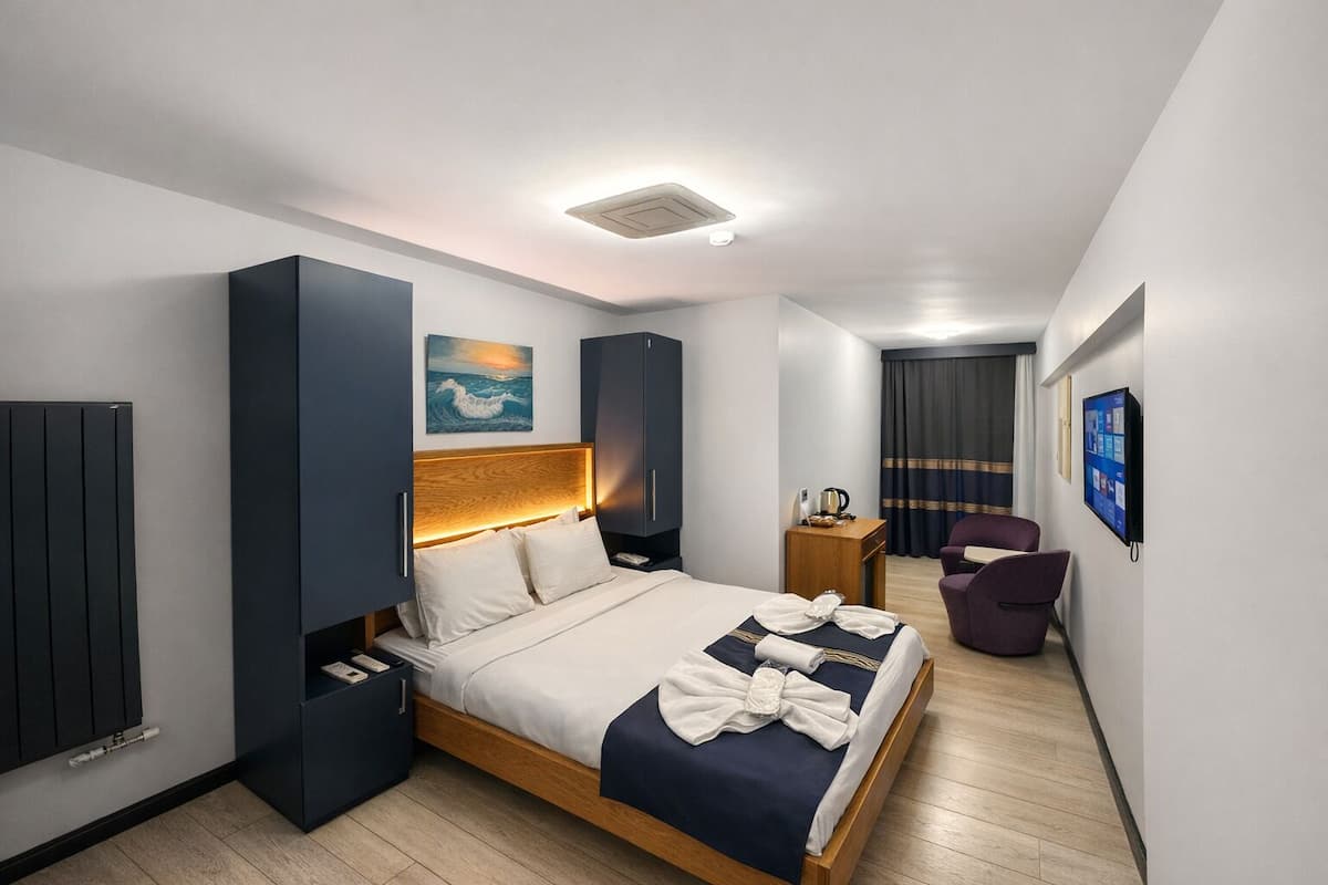 A modern hotel room with a bed, a desk, a chair, a TV, and a painting on the wall.