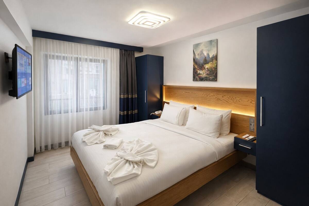 A hotel room with a large bed, a flat-screen TV, a painting on the wall, and a nightstand with a phone.