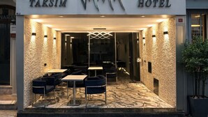 HOTEL TAKSIM con fachada moderna, ventanas de diseño hexagonal y una entrada bien iluminada con mesas al aire libre.