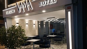 Exterior del HOTEL VAMA con un diseño moderno, que presenta fachada de piedra, entrada de vidrio y zona de estar al aire libre con mesas y sillas.