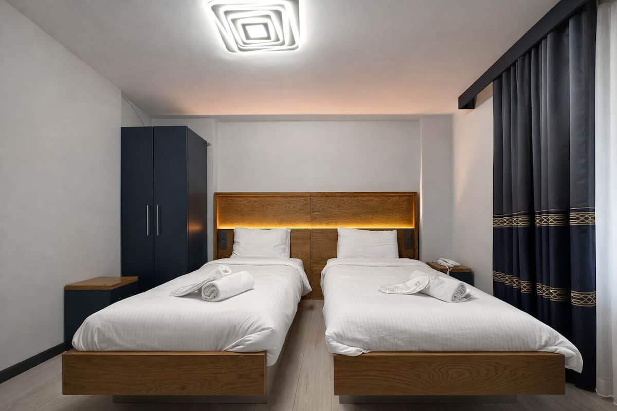 A double bed with wooden headboard, a nightstand, a wardrobe, and a curtain with a pattern.