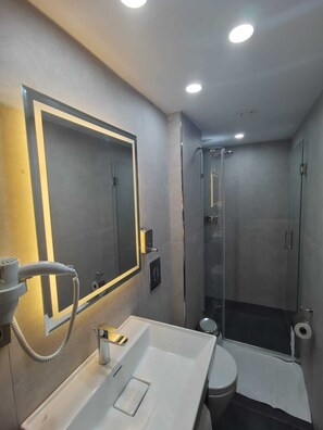 A modern bathroom with a large mirror, a sink, a toilet, and a glass-enclosed shower. - Vama Otel Taksim (Istanbul)