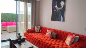 Un salon moderne avec un canapé rouge vif, une porte vitrée donnant sur un espace extérieur et un grand tableau encadré au mur.